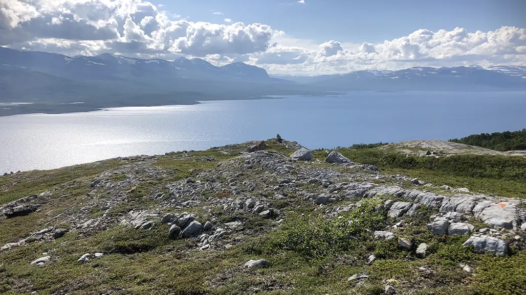 Gräs och sten, vatten och fjäll i bakgrunden. Foto