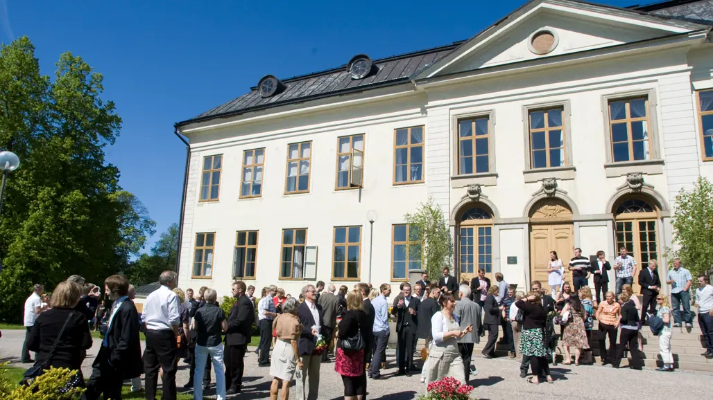 Herrgårdsliknande byggnad med folksamling framför en grönskande sommardag. Foto: Jenny Svennås-Gillner