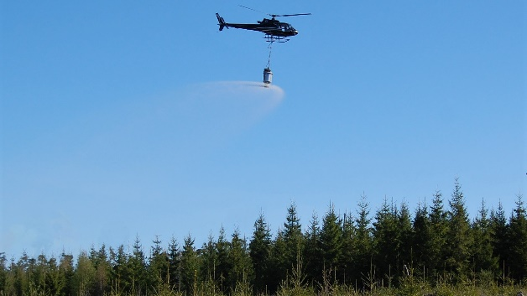 Bilden visar hur en helikopter sprider gödsel från luften