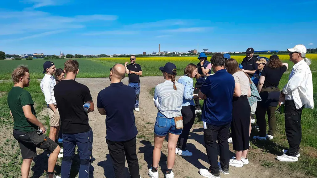 Många personer står på ett fält under en blå himmel. Foto.