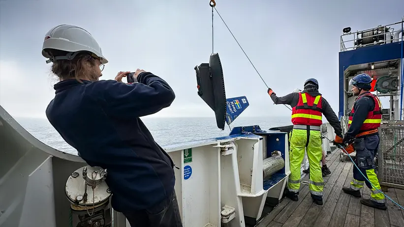 En liten segelbåt vinschas ner från forskningsfartyg