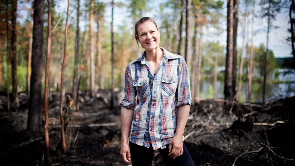En kvinna som står i skogen med ett leende på läpparna.