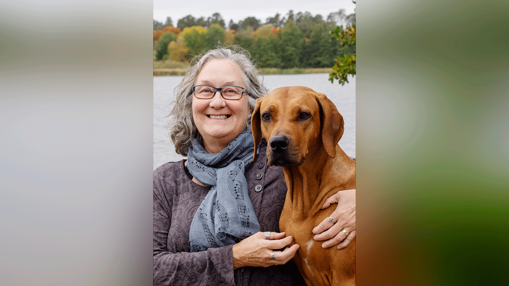 En kvinna som håller en hund framför ett vattendrag.