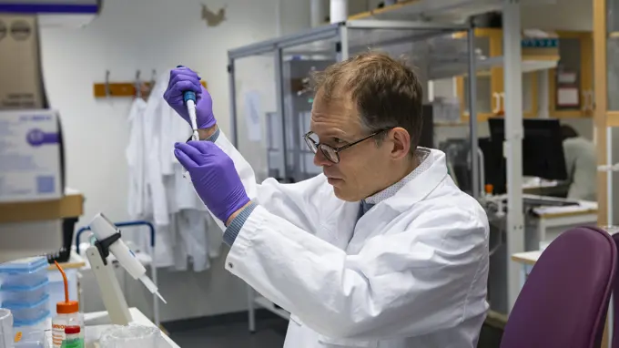 En person står i ett labb och pipetterar.