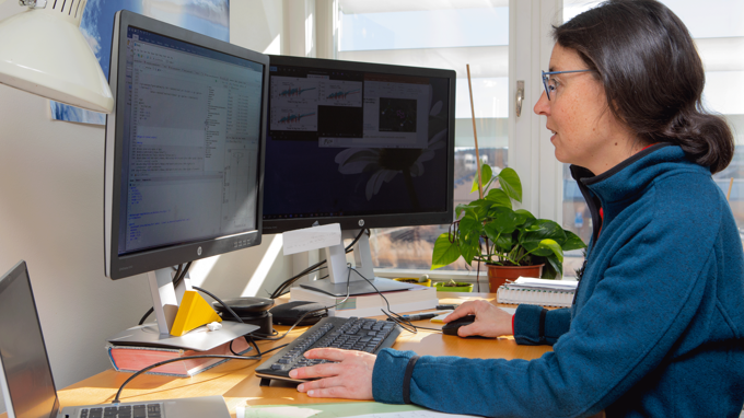 En kvinna med mörkt hår sitter framför datorn och programmerar.