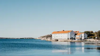 Bilden visar Havsfiskelaboratoriet i Lysekil utvändigt. Byggnaden har en vit/blå fasad och ligger vid havet. Solen skiner.
