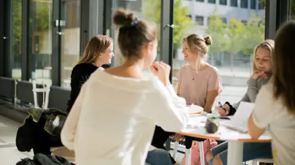 Studenter sitter runt ett bord och diskuterar